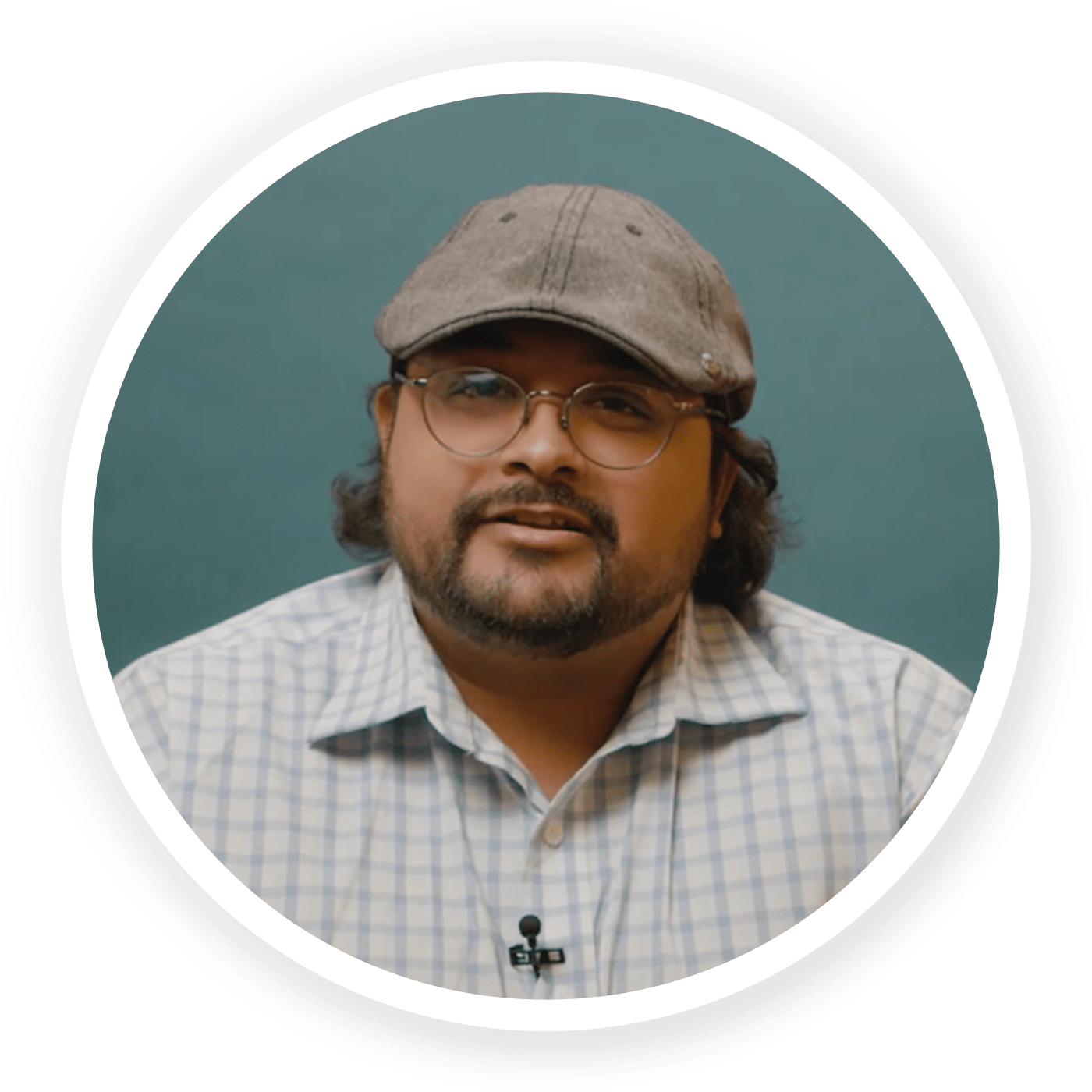 Profile of Vikaas Shanker in a light-blue, checkered shirt, grey flat cap hat on a dark blue-green background
